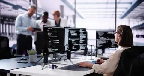 woman coding on multiple monitors