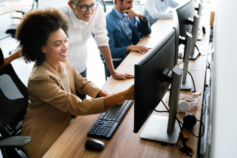 Two smiling women using AI tools at a computer in the office
