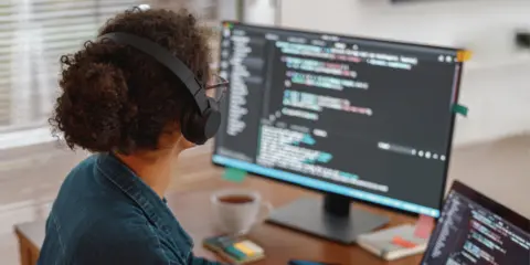 Programmer coding with a monitor and an open laptop side by side